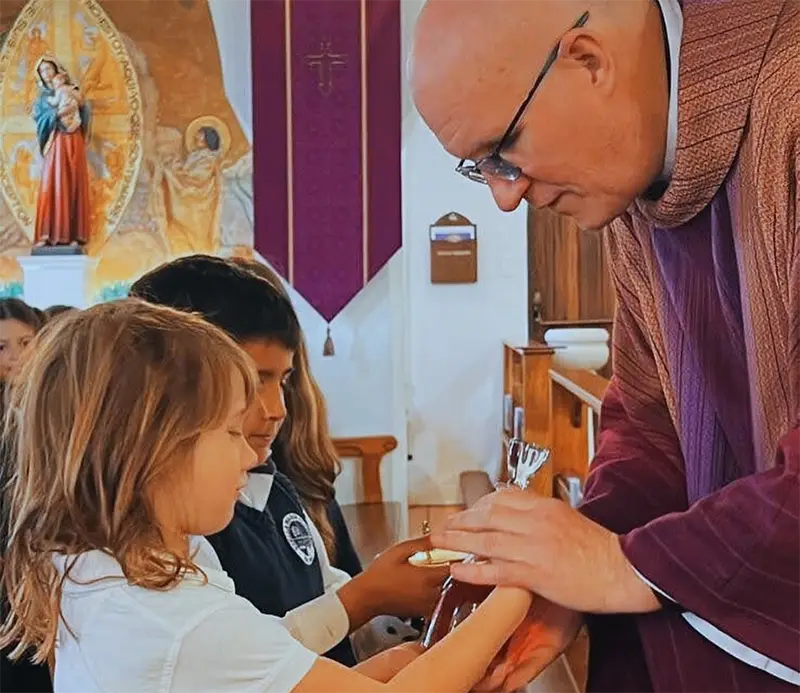 Students giving bread and wine to the priest during offertory at Mass